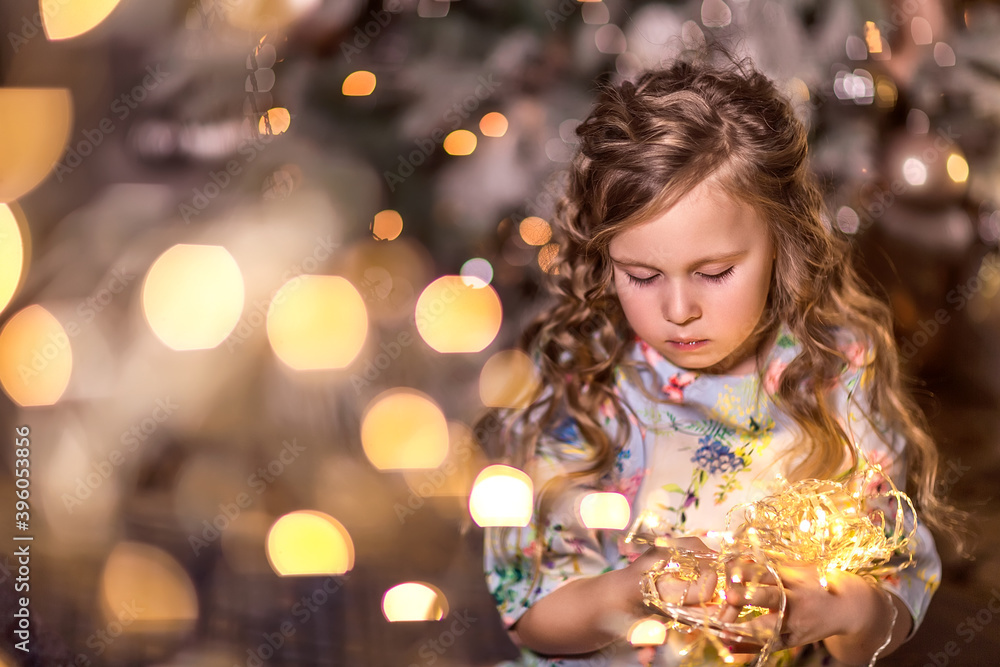 Portrait of a beautiful laughing girl with curly long hair on a background of blurred Christmas lights (bokeh) and a Christmas tree.