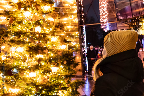 Beautiful blonde hair Caucasian girl with hat standing in front of a beautiful Christmas tree 