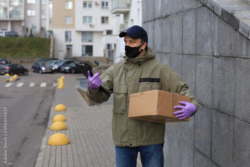 Courier in face mask with a parcel at the entrance of home verifies the information in the documents.