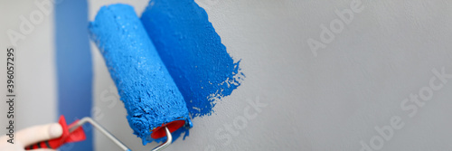 Hand holds roller and wire on wall with blue paint. Low roller performance. Convenient and versatile tool for painting walls. Tools with which best lay paint on surface. DIY repair in apartment