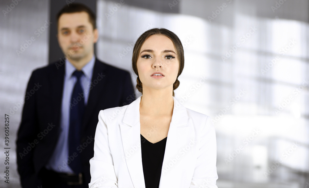 Young beautiful businesswoman is standing in an office with a male colleague at the background. Concept of success in a business Young beautiful businesswoman is standing in an office with a male colleague at the background. Concept of success in a business