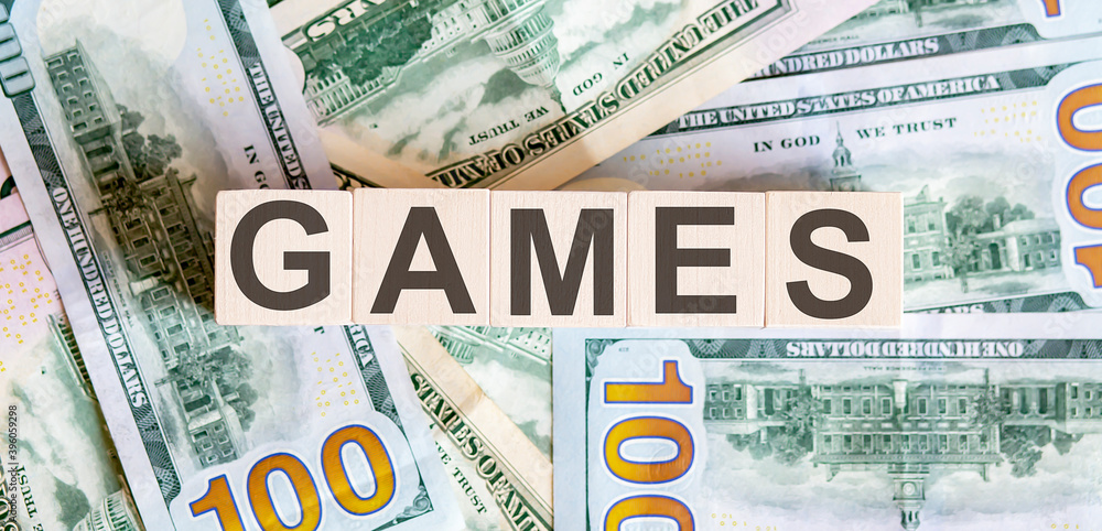 Concept words GAMES on wooden blocks on a beautiful background from dollar bills. Concept words GAMES on wooden blocks on a beautiful background from dollar bills.
