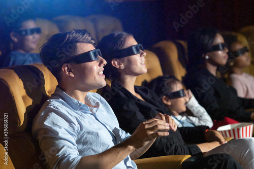 3D Movie. Young cacasian man and friends watching movie in cinema theater with popcorn and drinks.