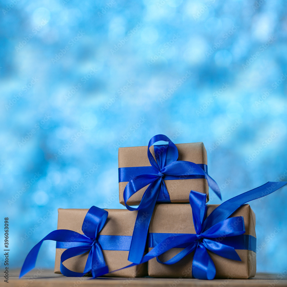 Christmas gift boxes with blue ribbons against blue lights garland and bokeh background. Holiday greeting card. Square image Christmas gift boxes with blue ribbons against blue lights garland and bokeh background. Holiday greeting card. Square image