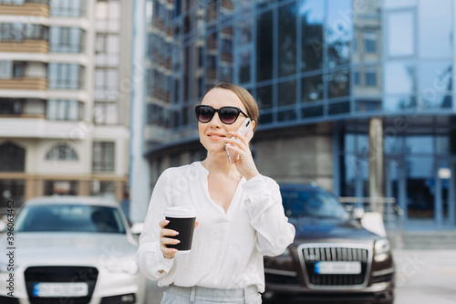 A business woman walking down the street in a business district talking on the phone.