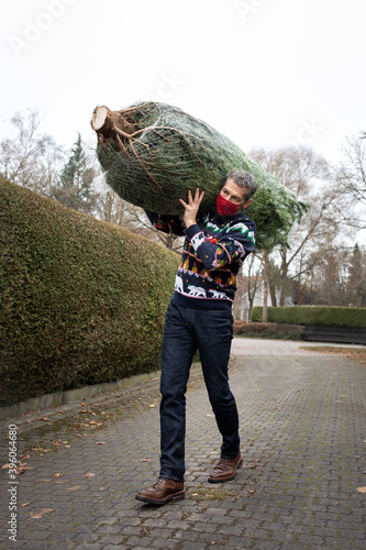 Man with face mask carrying a Christmas tree that he picked and cut himself