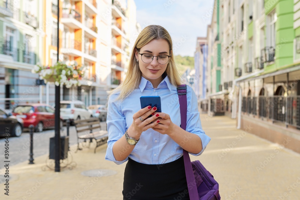Fototapeta premium Business woman in glasses in blue shirt with laptop bag using smartphone
