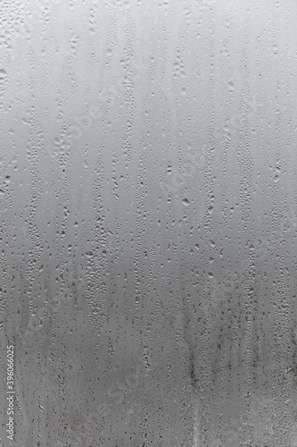 Natural drops of water flow down the glass, high humidity in the room, condensation on the glass window. Neutral colors. Vertical photo orientation