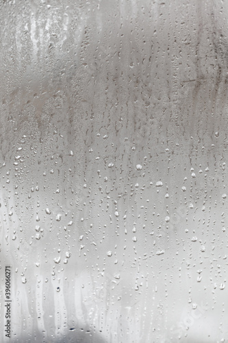Natural drops of water flow down the glass, high humidity in the room, condensation on the glass window. Neutral colors. Vertical photo orientation