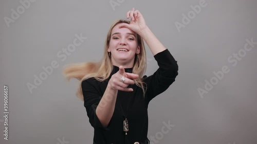 Showing loser sign, displaying dud gesture, alpha. Two fingers 2, disgust on face, negative human emotion facial expression. Young attractive woman, dressed black sweater with green eyes, blonde hair