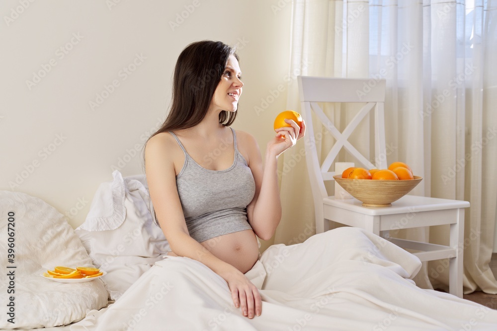 Young beautiful pregnant woman eating oranges sitting in bed at home Young beautiful pregnant woman eating oranges sitting in bed at home
