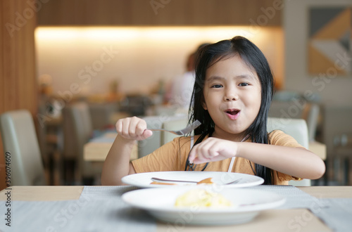 Asian child cute or kid girl smile holding fork to enjoy eating delicious food to hungry on white dish and table with happy for lunch or breakfast and appetizing in morning at restaurant or food court