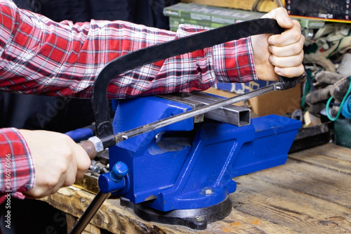 A worker is cutting by hacksaws metal profile. A handyman with hacksaws for metal. A locksmith vise