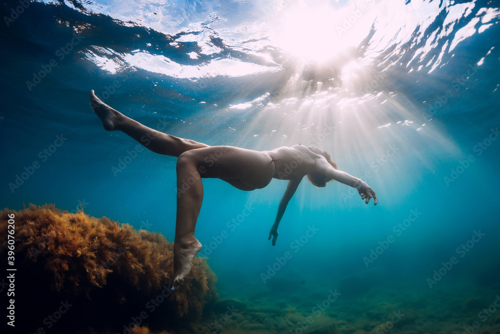 Slim woman posing underwater. Attractive girl glides in sea with sunlight