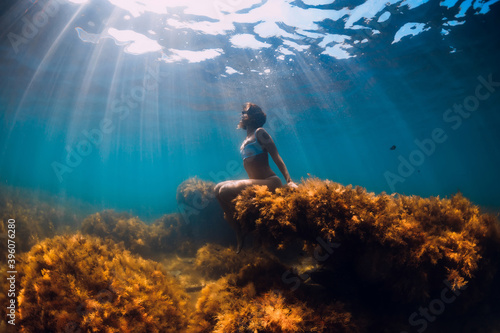 Attractive woman posing and sitting at sea bottom underwater. Freediver in sea