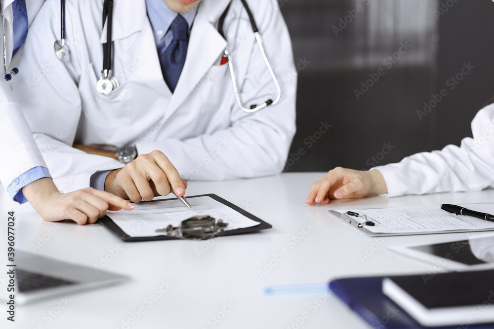 Group of unknown doctors are sitting at the desk and discussing problems or disease treatment in modern hospital office. Coronavirus countering, patient help in medicine concept Group of unknown doctors are sitting at the desk and discussing problems or disease treatment in modern hospital office. Coronavirus countering, patient help in medicine concept