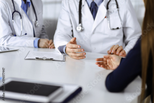 Two doctors and patient woman discussing something while sitting at the desk in modern clinic. Perfect medical service, medicine concept during Coronavirus pandemic. Covid 2019