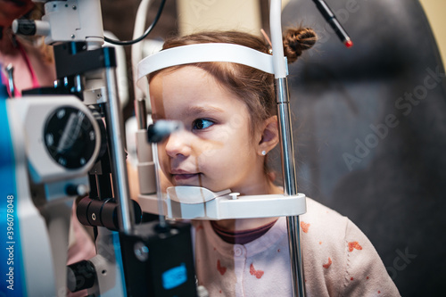 Fototapeta Naklejka Na Ścianę i Meble -  Beautiful and adorable little girl receiving ophthalmology treatment. Doctor ophthalmologist checking her eyesight with modern equipment.
