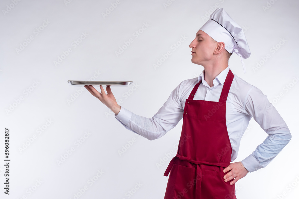 Chef is holding an empty tray. Man chef with a metal toe cap in his hands. Chef on a white background. Concept - he demonstrates a dish. The cook shows something. Man in cook uniform. Chef is holding an empty tray. Man chef with a metal toe cap in his hands. Chef on a white background. Concept - he demonstrates a dish. The cook shows something. Man in cook uniform.