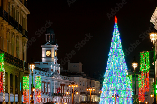 Árbol de navidad en la Puerta del sol en Madrid, España. Iluminación navideña de la plaza desde calle Alcalá, donde se puede ver el Palacio de correos con su reloj y el árbol de navidad.  28/11/2020. photo