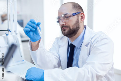 Genetic scientist conducting pharmacology exepriment, Researcher in biotechnology sterile lab holding analysis in tube wearing gloves and protection glasses.