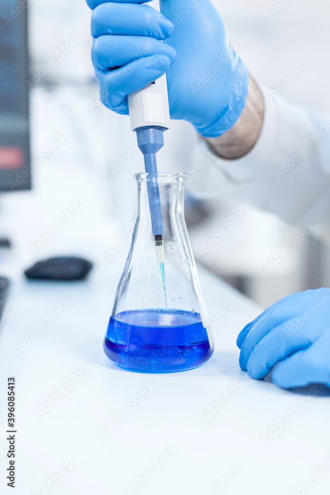 Fototapeta premium Scientist holding dispenser on test tubes in clinic pharmacy and medical research laboratory. Senior professional chemist using pippete with blue solution for microbiology tests.
