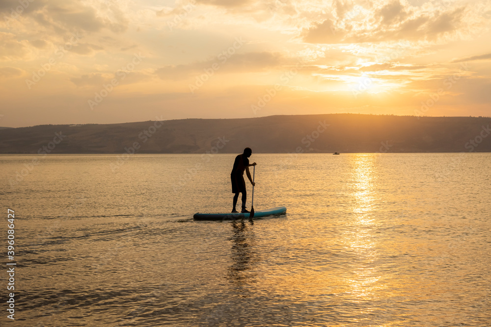 Man sail on a SUP board in a large lake during sunrise. Stand up paddle boarding - active recreation in nature. The Sea of Galilee, Lake Tiberias, Kinneret, Kinnereth. High quality photo.
