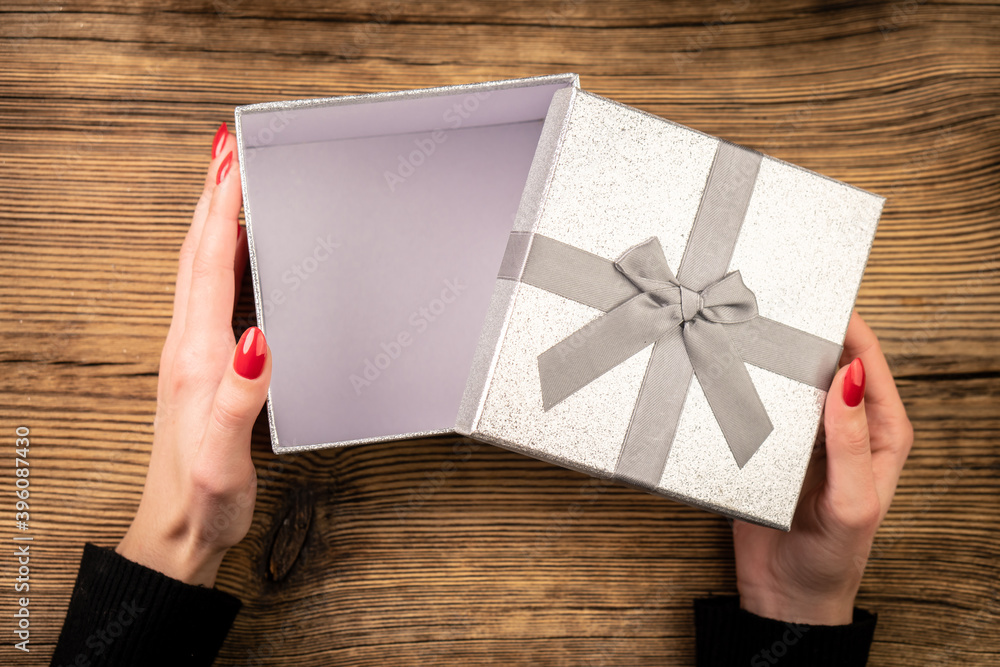 Top view of female hands opening gift box on wooden table. Top view of female hands opening gift box on wooden table.