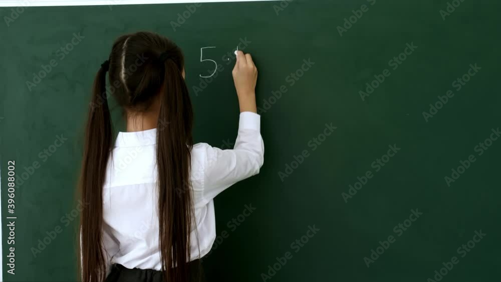 Little schoolgirl writing on chalkboard in classroom during math lesson Little schoolgirl writing on chalkboard in classroom during math lesson