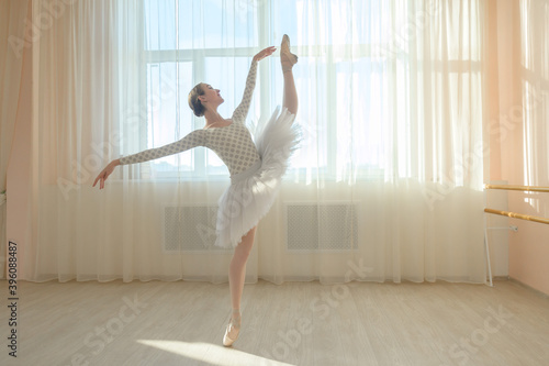 Fototapeta Naklejka Na Ścianę i Meble -  Beautiful ballerina in body and white tutu is training in a dance class. Young flexible dancer posing in pointe shoes.