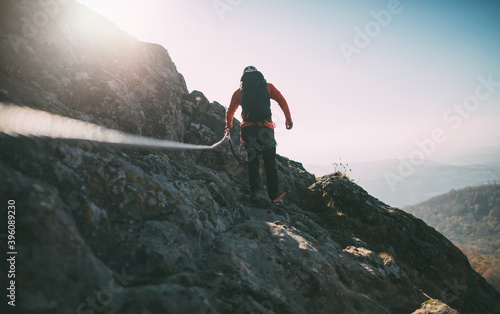 Rear view of man with backpack climbing a mountain using rope photo
