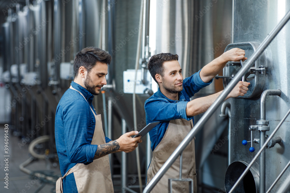 Worker in uniform looking at tablet standing in drink factory Worker in uniform looking at tablet standing in drink factory