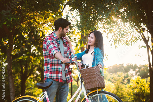 Couple Caucasian man with Asian woman lead bicycles in the park, romantic, dating.