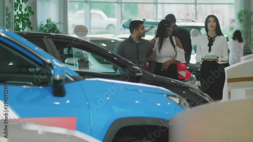 A young emotional African-American couple chooses a new car, a sales Manager stands nearby, selective focus.