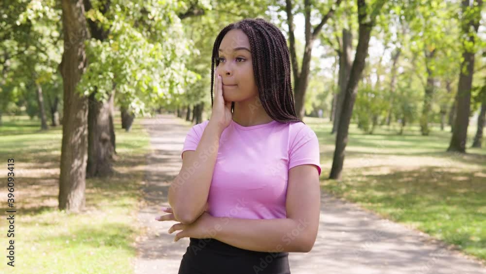 A young black woman acts frustrated in a park on a sunny day