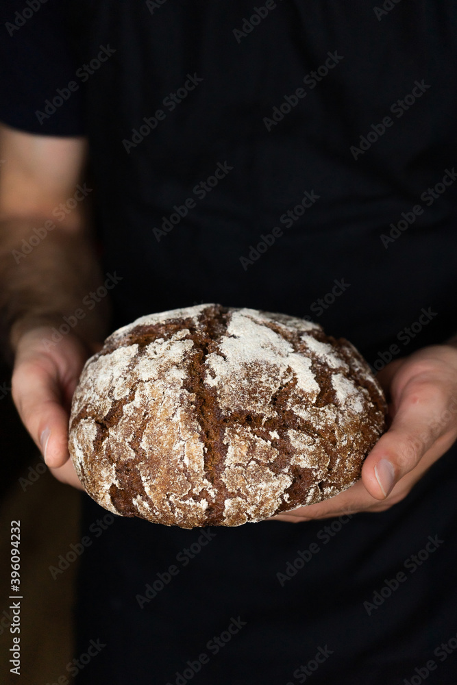 Round rye bread in the hands of men. Baker and hot baked goods.