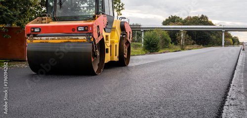 Asphalt road roller with heavy vibration roller compactor press new hot asphalt on the roadway on a road construction site. Heavy Vibration roller at asphalt pavement working. Repairing.