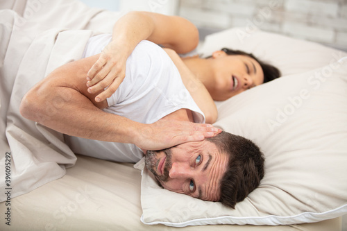 man covers his ears as wife snores loudly