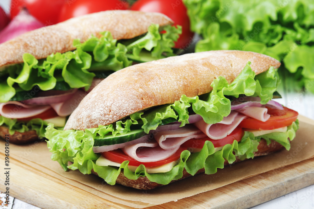Two sandwiches with fresh vegetables, ham and cheese in ciabatta bread Two sandwiches with fresh vegetables, ham and cheese in ciabatta bread