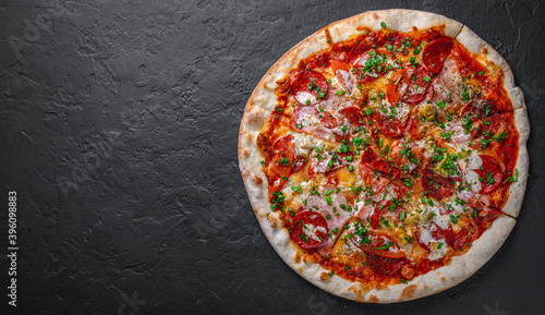 Pizza with Mozzarella cheese, ham, tomato sauce, pepper, salami. Italian pizza on Dark grey black slate background