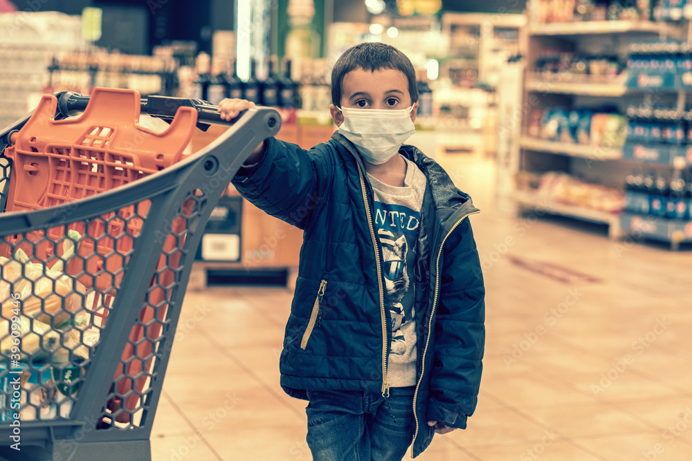 Obraz premium Boy wears protected mask in store. Shopping time during coronavirus outbreak. Boy in a medical mask. Shopping with kids during virus outbreak. Boy in face mask in supermarket. toned