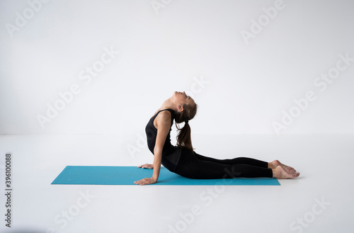 Young woman practicing yoga, lying and stretching in Cobra pose, doing Bhujangasana exercise. Attractive girl in black sportswear. Beautiful sporty fit yogini woman practices yoga asana bhujangasana.