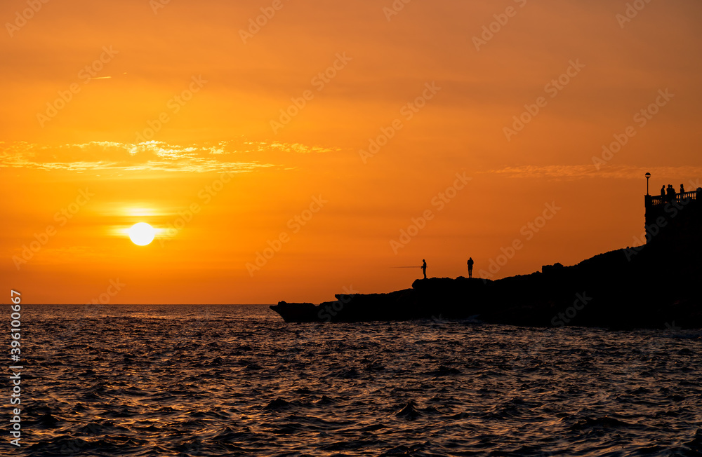 A fisherman silhouetted against the setting Mediterranean sun