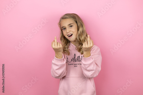Young beautiful child girl standing over isolated pink background showing middle finger doing fuck you bad expression, provocation and rude attitude. screaming excited photo