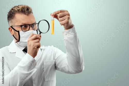 The doctor looks at a test tube with liquid through a magnifying glass, loupe. Scientific research concept, vaccine invention, COVID-19. copy space.