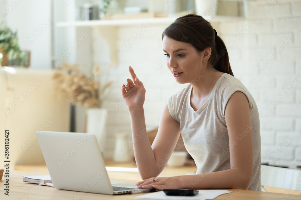 Focused young woman working online, using laptop, sitting at table in modern kitchen, confident female making video call, chatting, calculating bills, finances, checking financial documents Focused young woman working online, using laptop, sitting at table in modern kitchen, confident female making video call, chatting, calculating bills, finances, checking financial documents