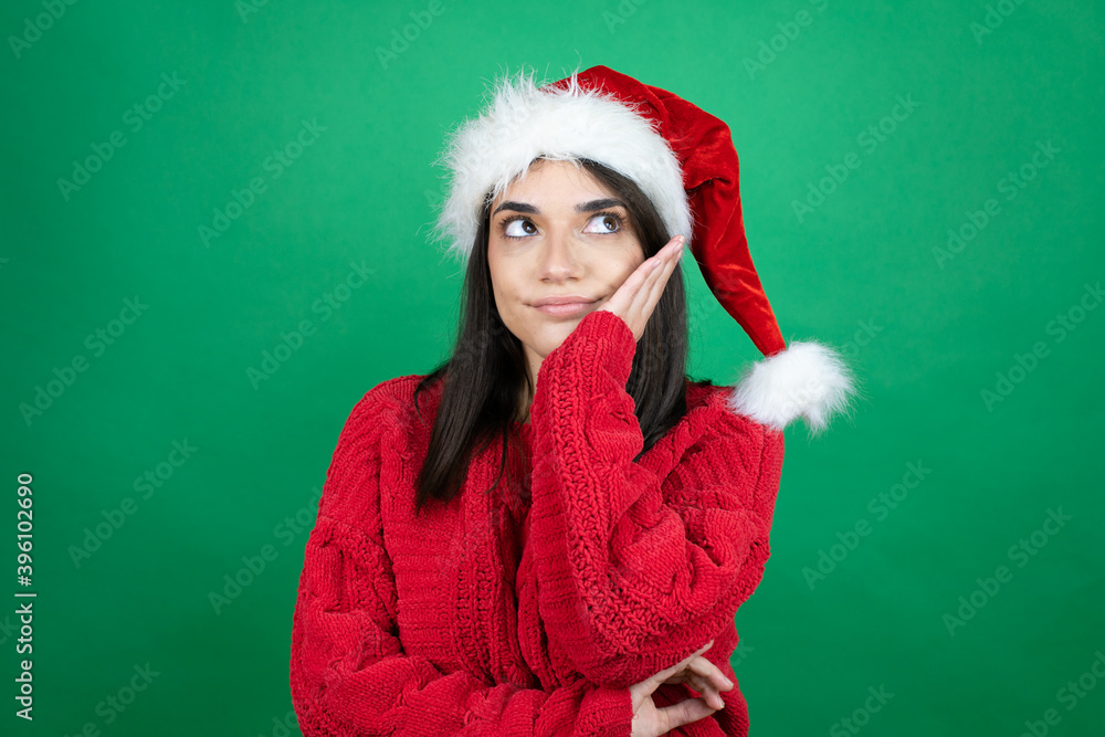 Young beautiful woman wearing Christmas Santa hat over isolated green background thinking looking tired and bored with crossed arms Young beautiful woman wearing Christmas Santa hat over isolated green background thinking looking tired and bored with crossed arms