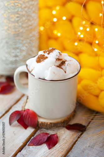 Delicious drink for cold autumn days: hot chocolate or latte with whipped cream and cinnamon. Cozy calm home atmosphere of lazy weekend morning. Yellow plaid and wooden table on background.