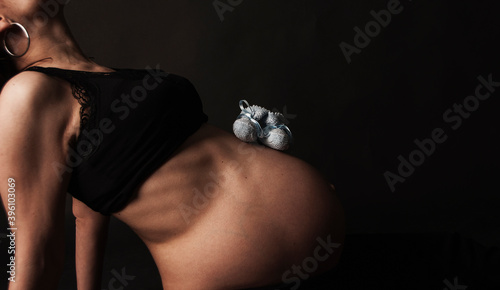 Barriga de embarazada con unos patucos de tela sobre fondo negro photo