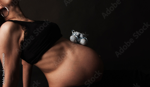 Obraz na płótnie Barriga de embarazada con unos patucos de tela sobre fondo negro